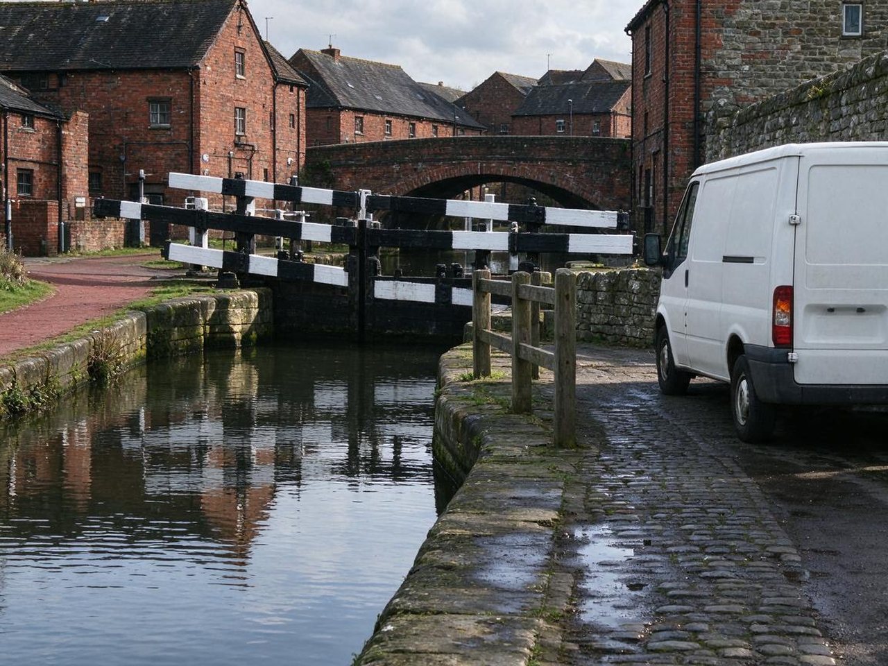 Canal lock with black-and-white gates and a white van parked on the cobbled lane beside it in Middlewich